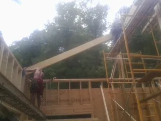Carpenter raising a rafter beam on a new second story frame in Edgar