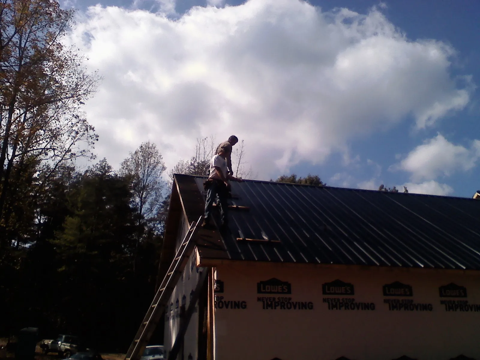 Roofer fastening dark metal panels high against a cloudy sky, from a Roof Inspection job in Edgar