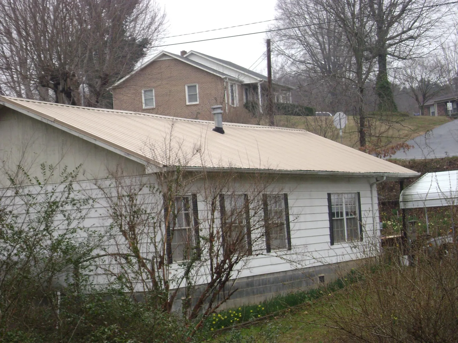 Tan metal roof on a white sided house set into a hillside — Commercial Roofing by Roofing Brothers in Edgar