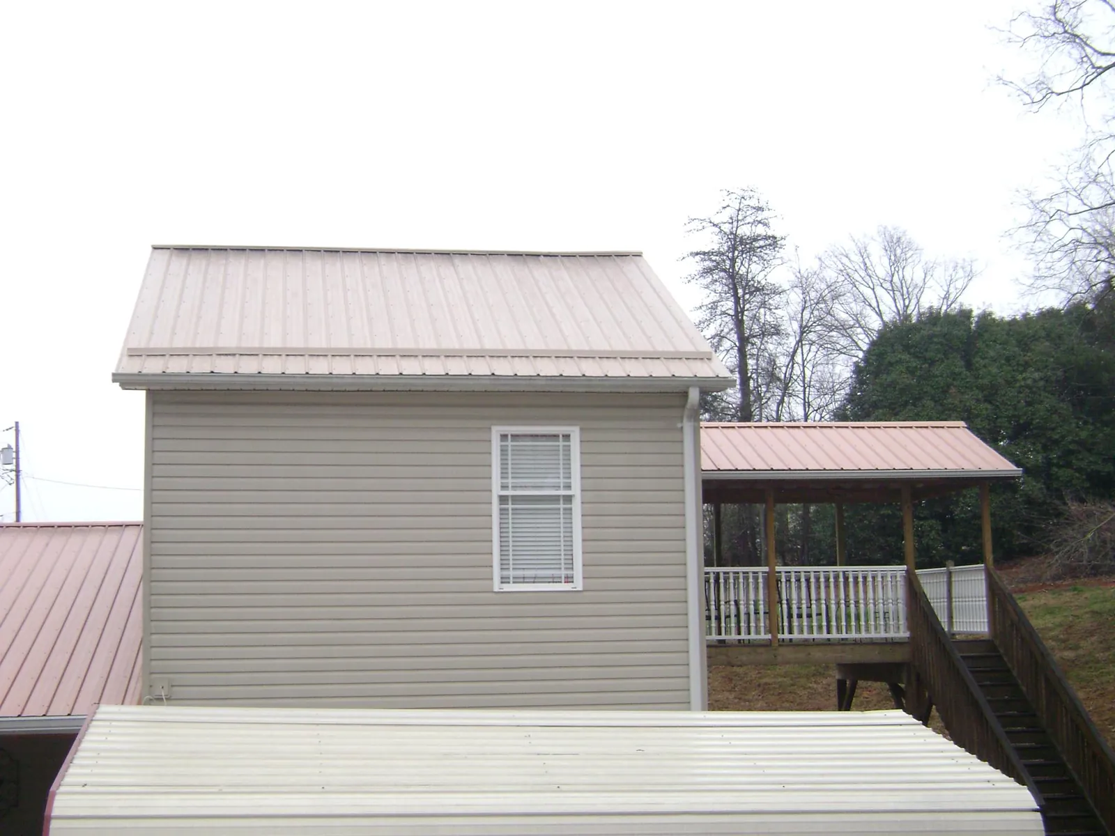 Tan metal roofs on a two story addition and attached porch, from a Roof Replacement job in Edgar